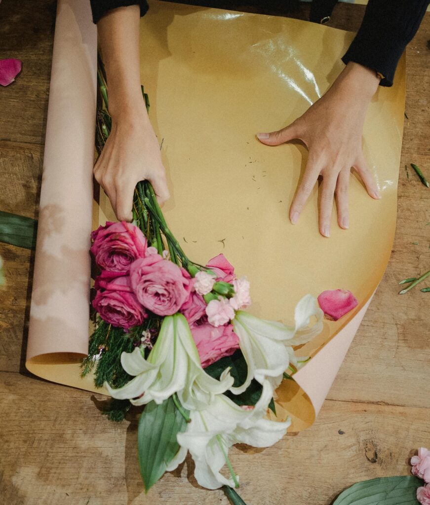 From above of crop anonymous female florist holding flowers and creating fresh bunch